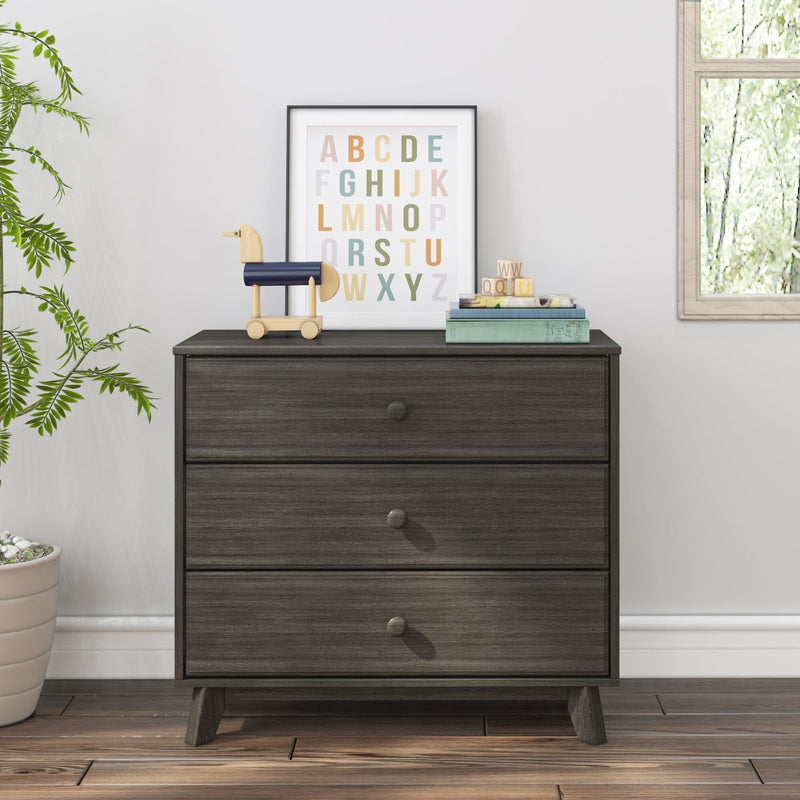 Dark wood three-drawer dresser in a children's room with framed colorful alphabet print, wooden toy horse, stacked books and letter blocks, potted plant and window