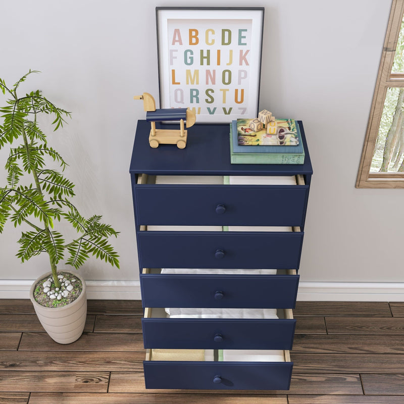 Navy blue five-drawer nursery dresser with open drawers showing folded baby clothes, wooden toy horse, framed alphabet print, children's books and potted plant on hardwood floor