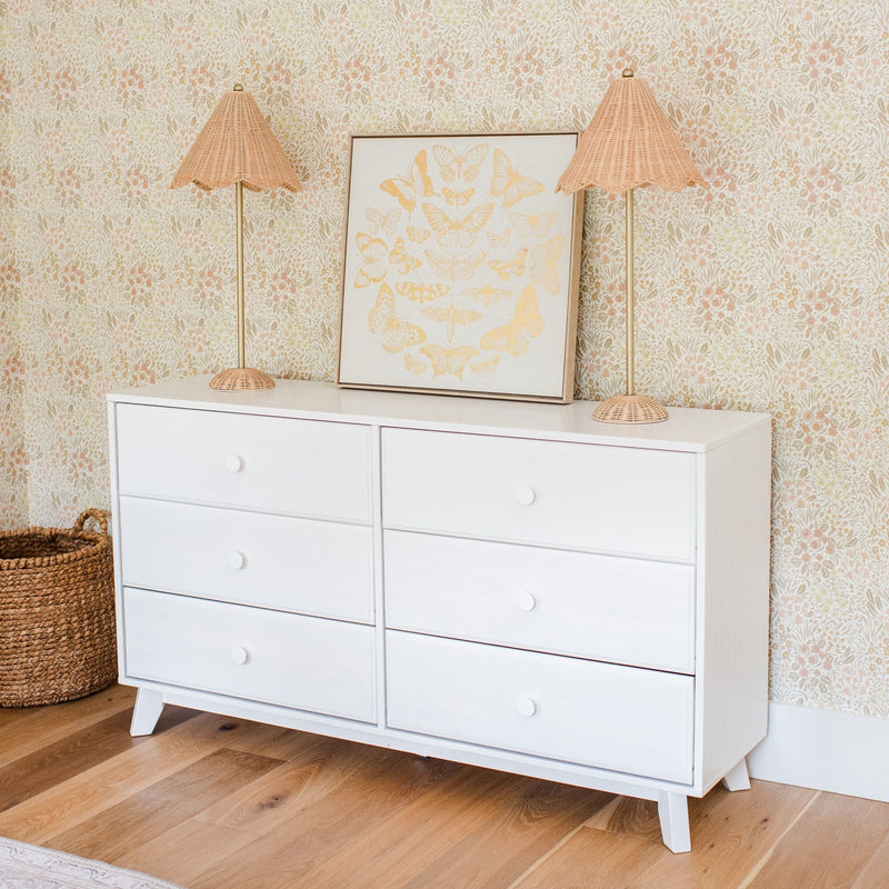 White six-drawer dresser on hardwood floor with rattan lamps, framed butterfly print, floral wallpaper and woven basket