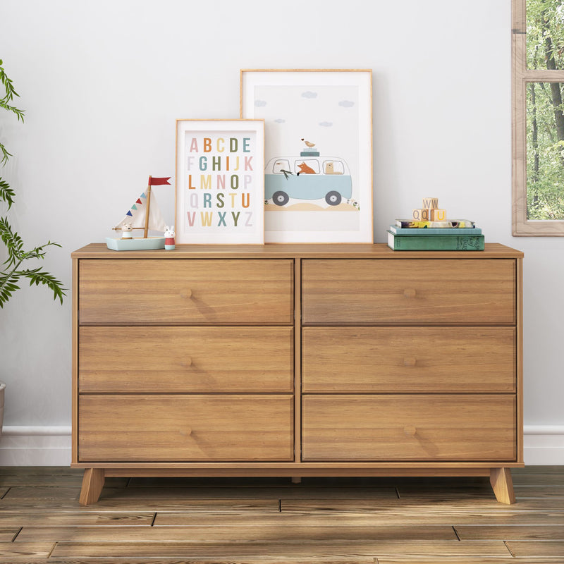 Mid-century modern natural wood six-drawer dresser in a child's nursery with colorful alphabet print, framed animal car art, toy sailboat, books and wooden blocks