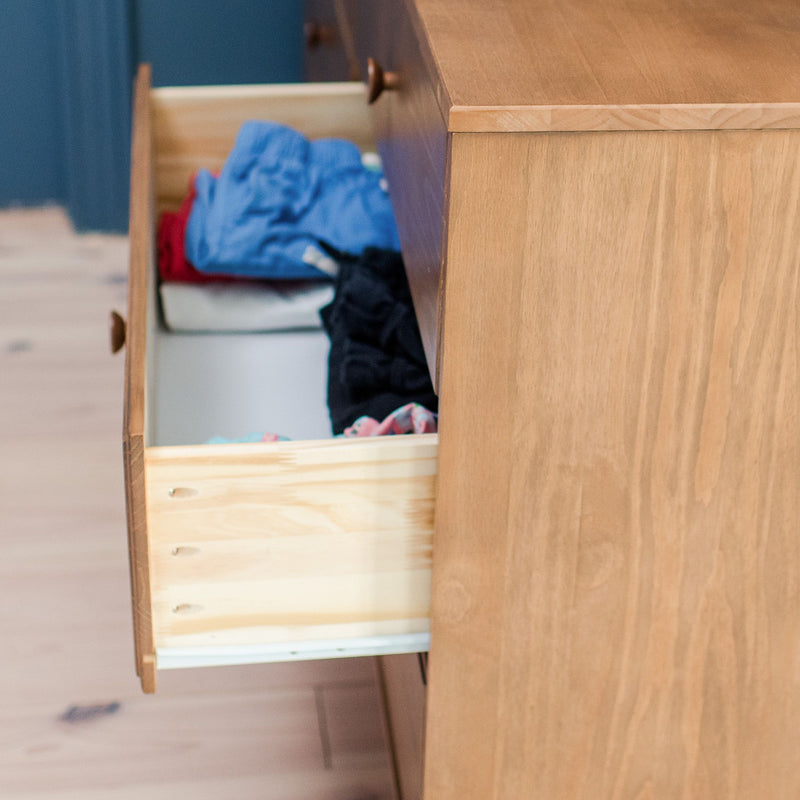 Open wooden dresser drawer with folded clothes (blue and black shirts) in bedroom on light hardwood floor