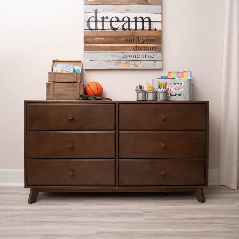 Mid-century modern dark wood six-drawer dresser in kids' room with rustic "dream" wall sign, toy basketball, wooden crates and art supplies