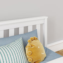 White wooden bed frame with blue and striped pillows and a yellow round pillow with smiley face, in a modern bedroom setting.