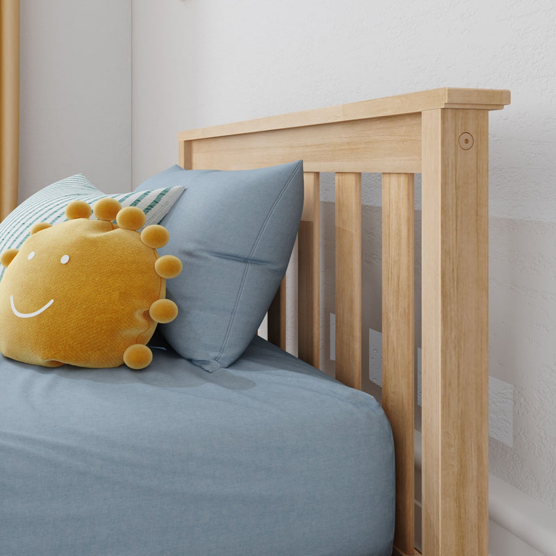 Natural wood baby crib headboard with slatted design, soft blue pillows and striped bedding, yellow sun plush toy in minimalist nursery decor