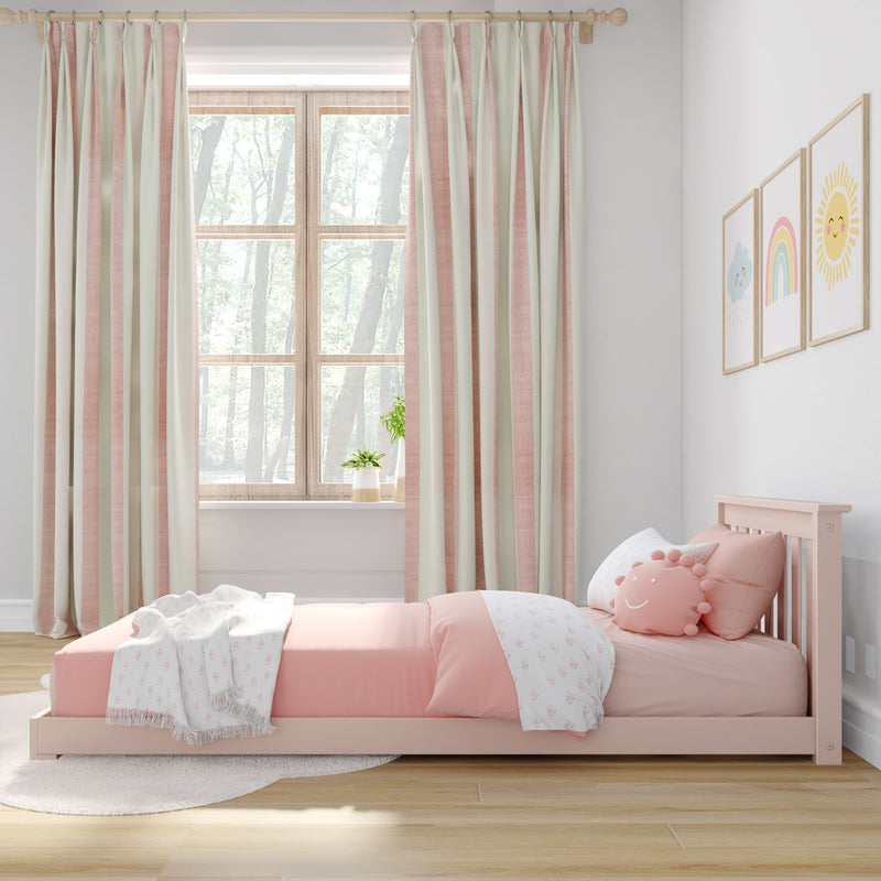 Pastel pink toddler bed with smiley sun pillow and patterned blanket, pink-and-cream striped curtains framing a wooden window in a bright nursery