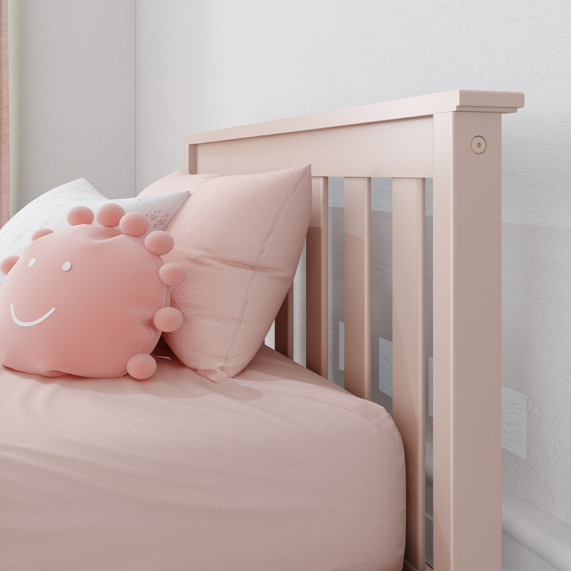 Pastel pink baby crib headboard with soft pink pillows and smiling pom‑pom cushion in a modern nursery