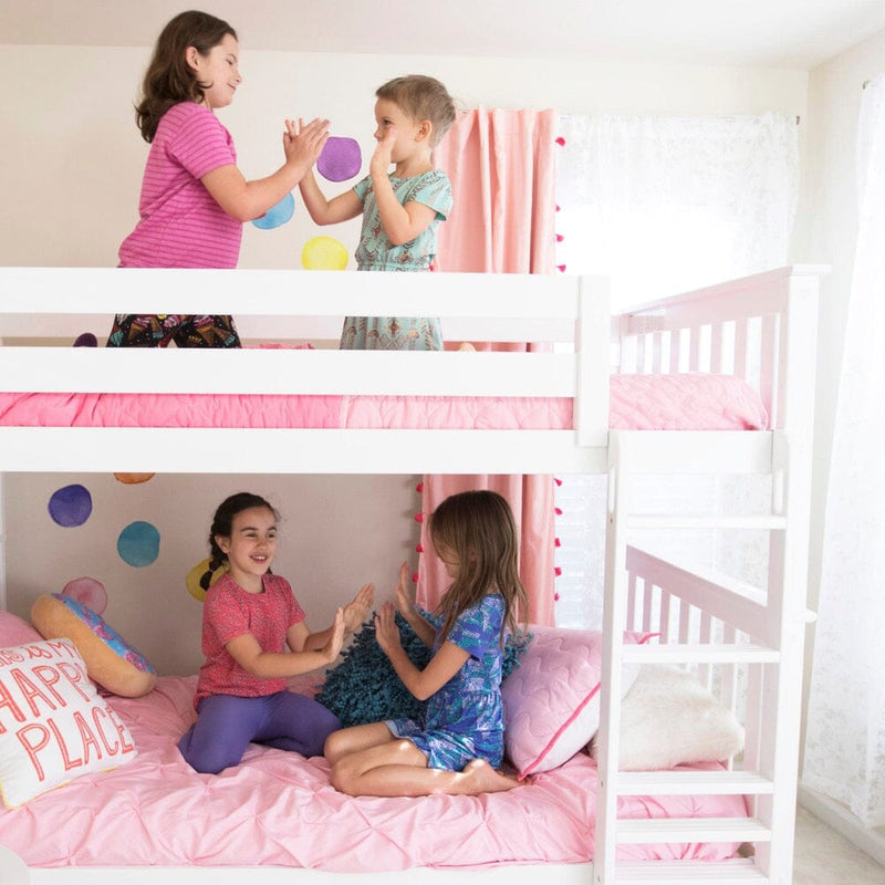 Four young girls playing a hand‑clap game on a white bunk bed with pink bedding and ladder in a bright, colorful children's bedroom