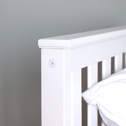 Close-up of white wooden slatted bed headboard with pillow on minimalist modern white bed frame