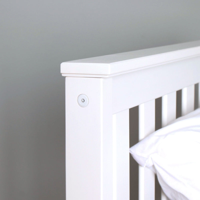 Close-up of white wooden baby crib railing and headboard detail in a modern minimalist nursery, slatted design with visible screw fitting