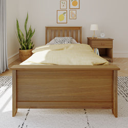 Minimalist Scandinavian bedroom: wooden single bed with yellow duvet and spotted pillow, wooden nightstand with lamp and clock, potted snake plant and framed fruit prints