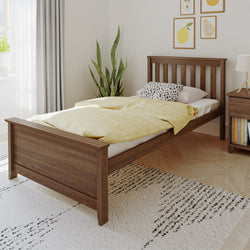 Minimalist wooden single bed with yellow duvet and spotted pillow in a bright modern bedroom with bedside table, indoor plant, and framed fruit prints