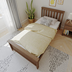 Cozy modern minimalist bedroom with single wooden bed, yellow duvet cover, black-and-white spotted pillow, wooden nightstand with lamp and books, potted snake plant, sheer curtains and light hardwood floor