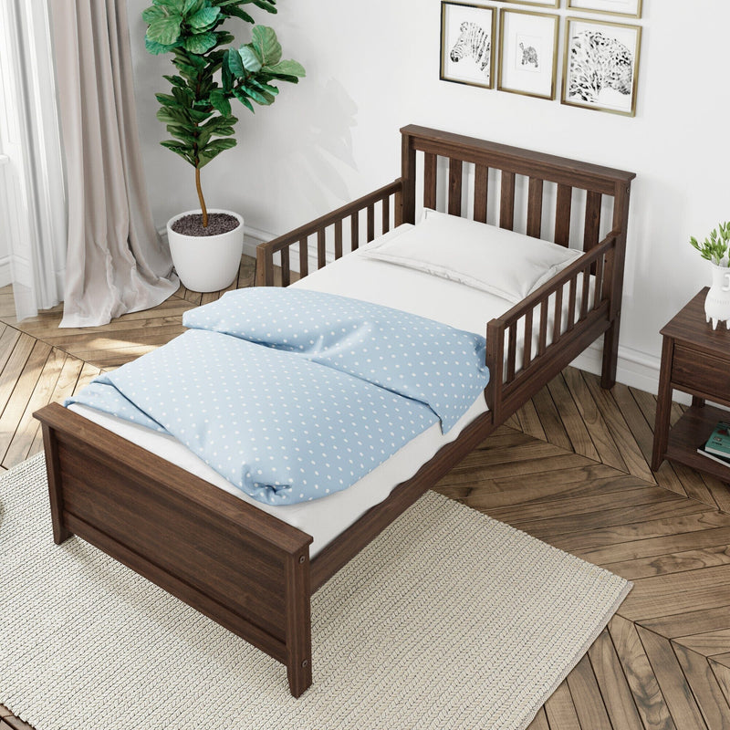 Dark walnut wooden toddler bed with safety rails and blue polka-dot duvet in a modern kids bedroom with herringbone hardwood floor, potted plant and nightstand