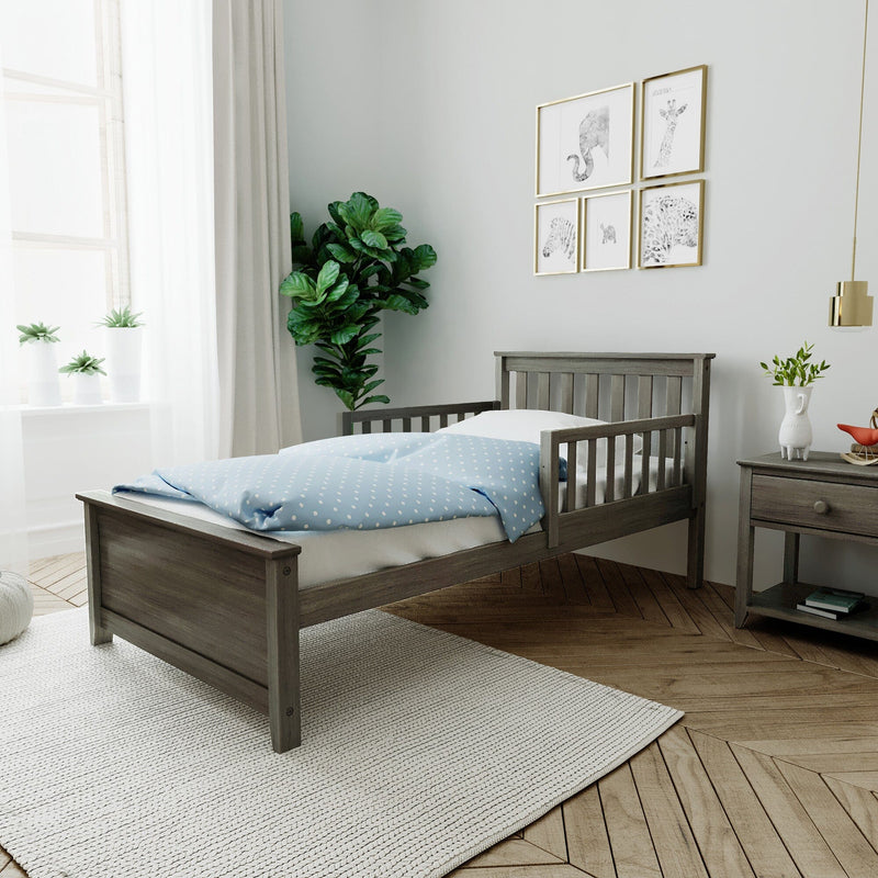 Bright neutral nursery with wooden toddler bed, blue polka-dot duvet, gray nightstand, gold-framed animal wall art, indoor plants and sheer curtains