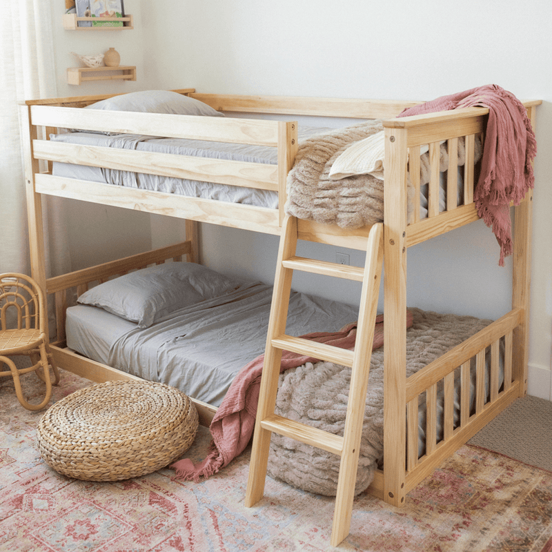 Natural pine bunk bed with ladder in a children's bedroom, gray bedding, pink throw and plush blanket, wicker pouf and vintage patterned rug