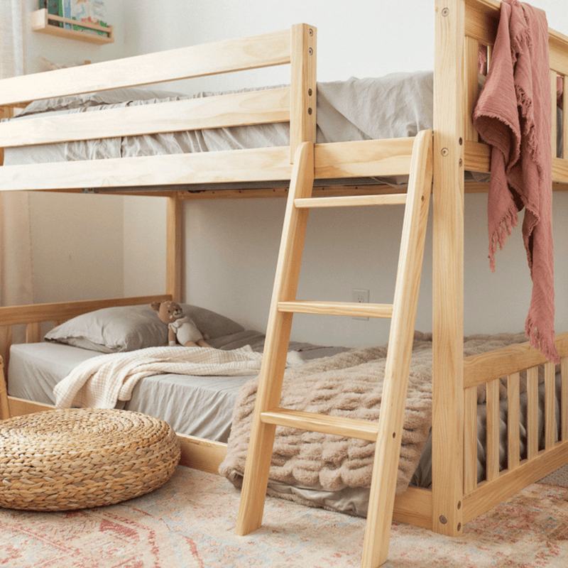 Natural pine wooden bunk bed with ladder in neutral kids' bedroom, soft gray bedding, plush doll, woven pouf and boho rug