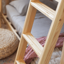 Close-up of natural pine wooden ladder for bunk bed in cozy boho bedroom with gray bedding, woven pouf, and textured throw