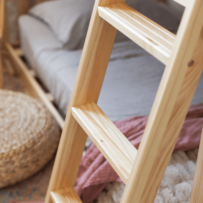 Close-up of natural pine wooden ladder for bunk bed in cozy boho bedroom with gray bedding, woven pouf, and textured throw