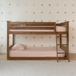 Wooden twin-over-twin bunk bed with ladder and blush-pink bedding in minimalist kids bedroom with patterned wallpaper