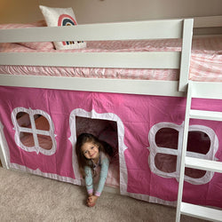 Child playing in pink playhouse bed with window curtains and ladder in cozy bedroom.