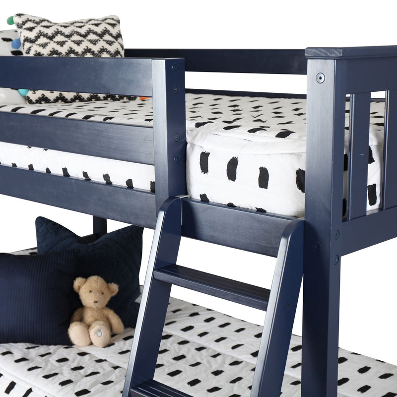 Navy blue wooden children's bunk bed with ladder, black-and-white patterned bedding, decorative pillows and a teddy bear