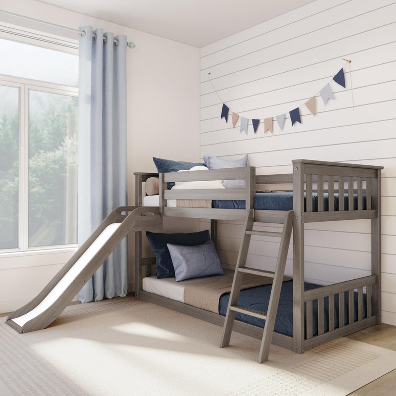 Gray wooden children's bunk bed with slide in a light coastal-style bedroom, navy and light-blue pillows, shiplap wall with pastel bunting and a large curtained window