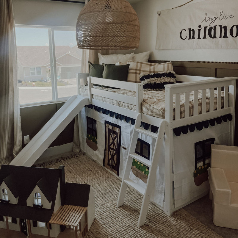 Neutral boho kids loft bed with slide and ladder, white wooden bunk with plaid and green pillows, playhouse curtains, woven rattan pendant light and dollhouse by a large window