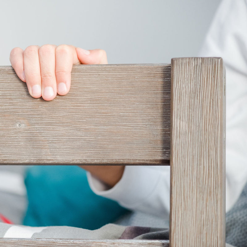 Child's hand grabbing wooden bed frame for support.