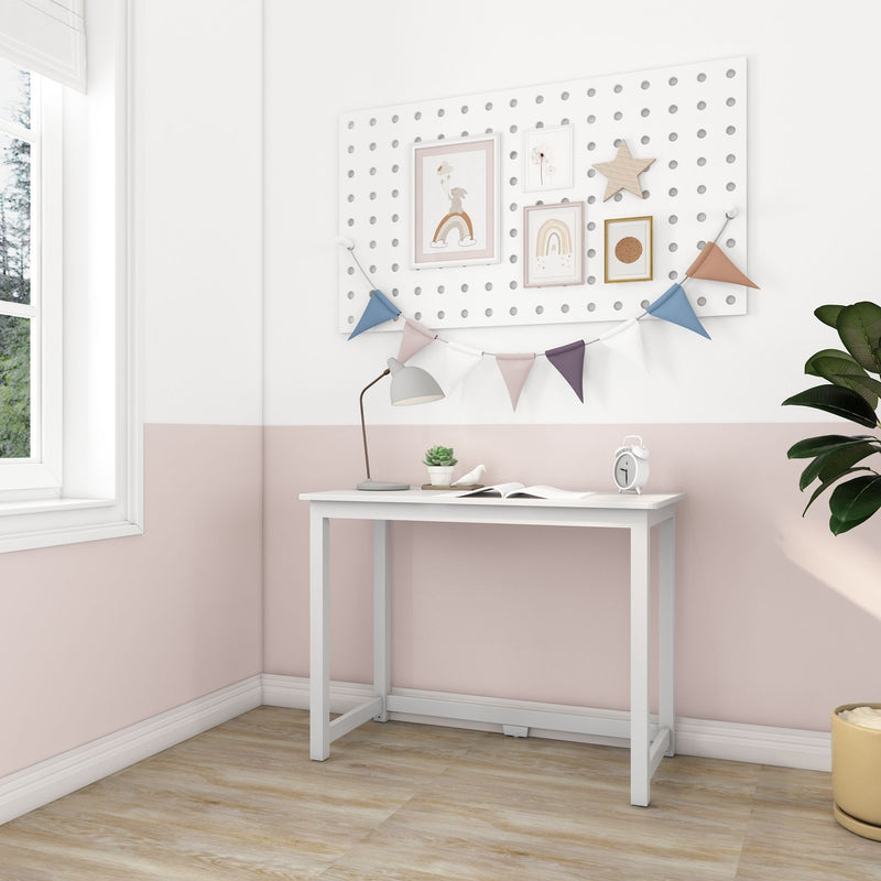 Pastel pink nursery and kids' room with a white desk, pegboard gallery wall featuring framed rainbow and bunny prints and a wooden star, pastel fabric bunting, gray desk lamp, succulent and white alarm clock