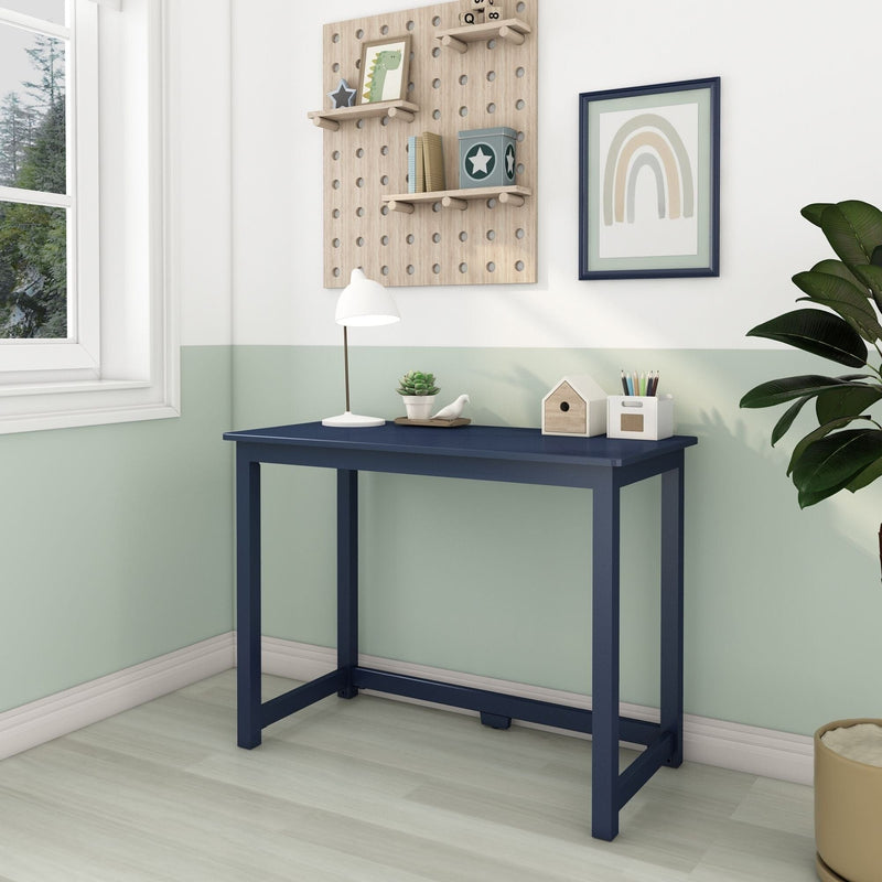 Minimalist home office corner with navy narrow writing desk under natural light, white desk lamp, succulent, pencil holder, pegboard shelves and framed rainbow wall art