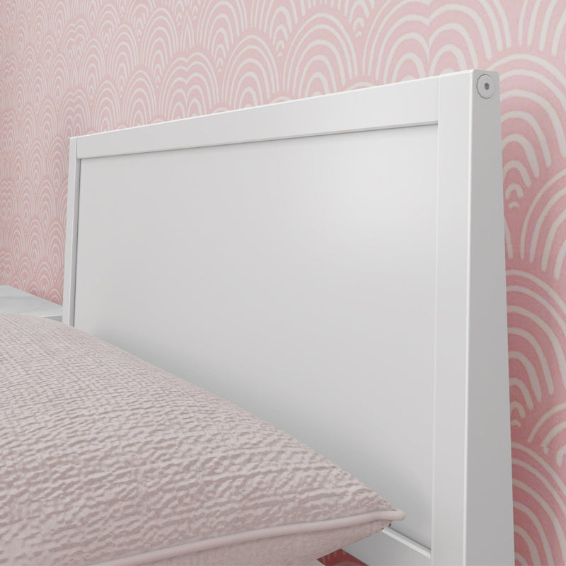 White wooden headboard against pink scallop-pattern wallpaper with blush quilted bedding in a modern bedroom