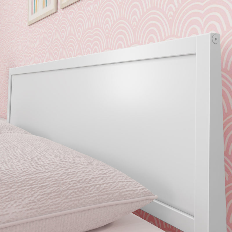 Close-up of white modern wooden headboard with blush quilted bedding against pink scallop-pattern wallpaper in a child's bedroom