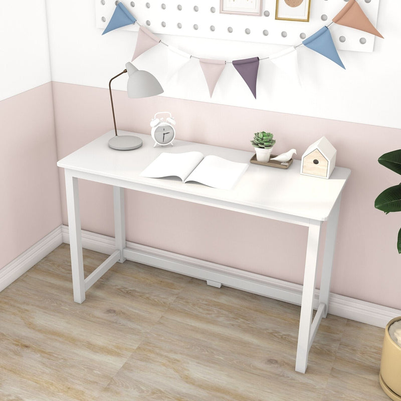 White minimalist writing desk against pink accent wall in a small home office with desk lamp, alarm clock, open notebook, succulent plant and decorative bunting on light wood floor
