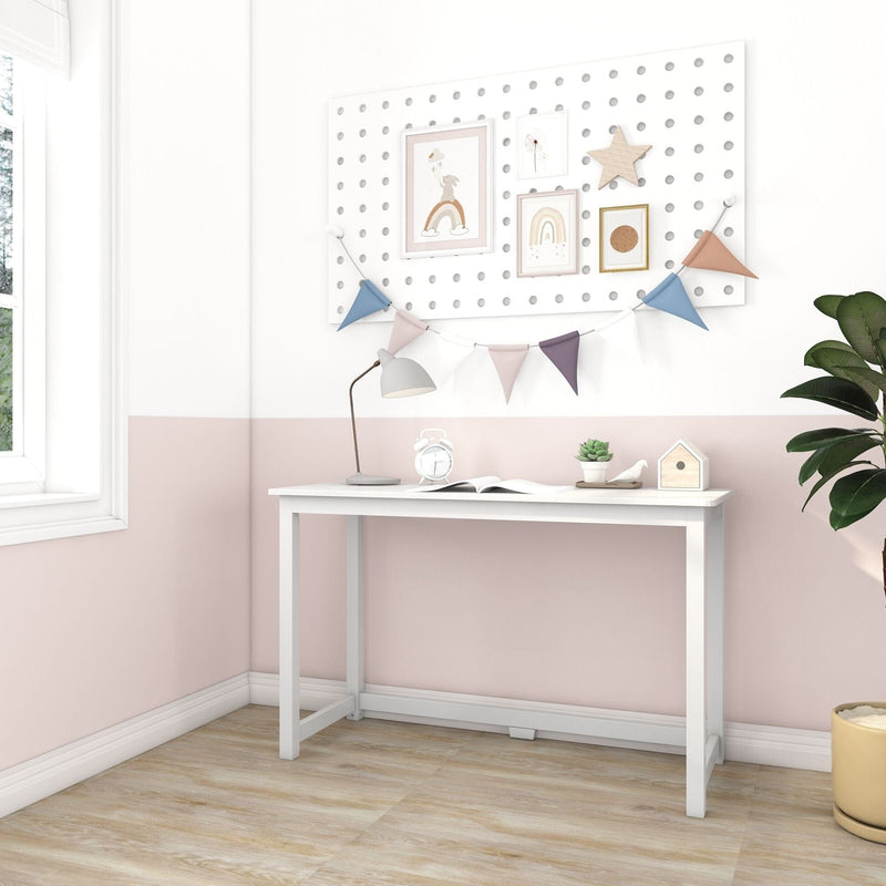 White kids desk in pastel pink nursery with pegboard art, pastel bunting garland, lamp, succulent and wood floor