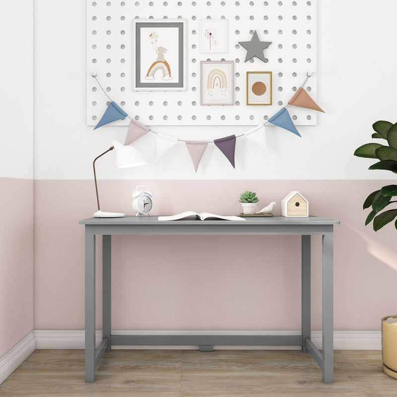 Modern pastel nursery study nook with grey desk, white desk lamp, alarm clock, open book, succulent and birdhouse on a pink-and-white wall decorated with bunting and framed rainbow art