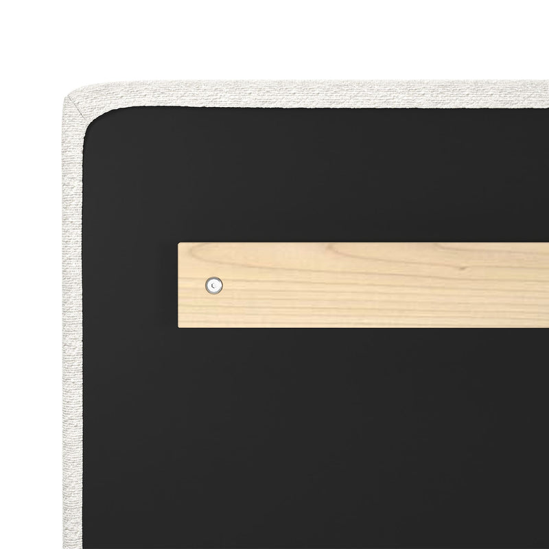 Close-up of an upholstered headboard corner showing white boucle fabric trim, black fabric panel and light wood mounting bracket with a visible screw