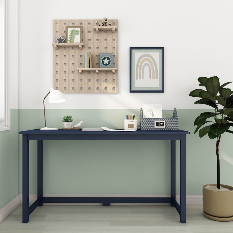 Children's study nook with navy desk and mint-green walls, wooden pegboard shelves holding toys and books, framed pastel rainbow print, white desk lamp and potted plant