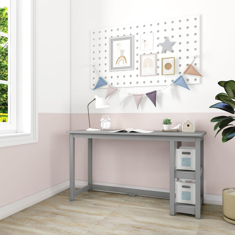 Kids study desk in a pastel nursery with pegboard wall decor, framed rainbow prints and bunting flags, white desk lamp, under-desk storage bins and potted plant by window