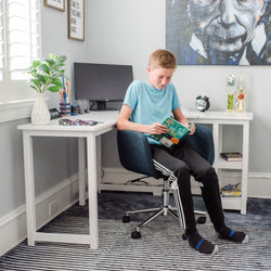 Boy reading a book in a study room with desk, computer, and wall art decor.