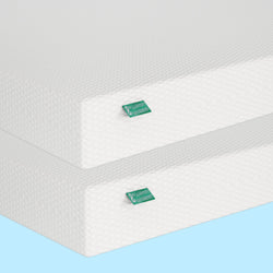Tall layers of high-density memory foam mattresses with textured white covers and green labels.