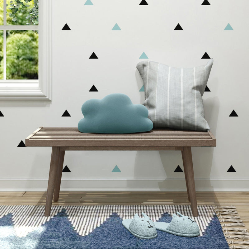 Modern nursery corner with wooden bench, blue cloud pillow, gray striped cushion, black and teal triangle wall decals, cat slippers on blue rug by window