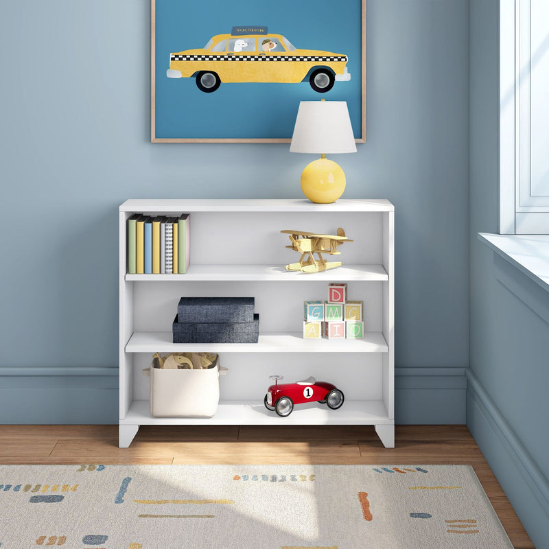 Kids room decor with white bookshelf, framed yellow taxi wall art, yellow table lamp, stacked books, wooden toy airplane, pastel alphabet blocks and red toy race car on a light blue wall