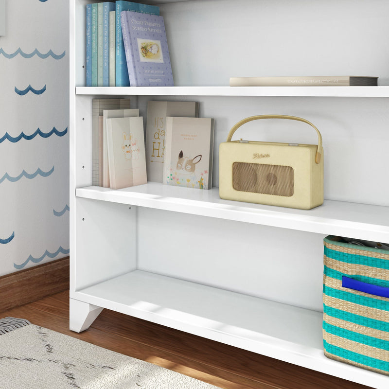 White bookshelf with children's books, a vintage radio, and a striped storage basket in a cozy room setting.