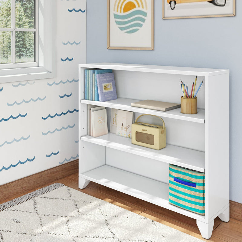 White wooden bookshelf in a children's room with colorful books, a woven basket, and decorative items on a wooden floor.