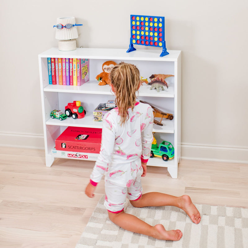 Child in pajamas playing near a bookshelf with toys and books in a colorful kids' room.