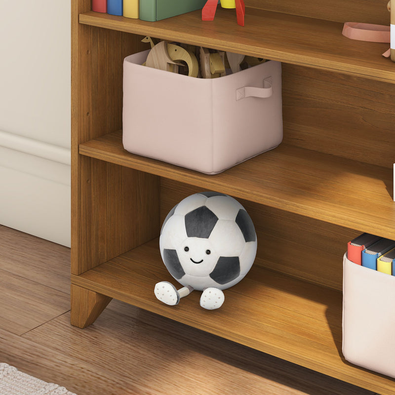 Kids room wooden bookshelf with pink fabric storage bin holding wooden toys and a smiling black-and-white soccer ball plush on the lower shelf, nursery storage and playroom organization