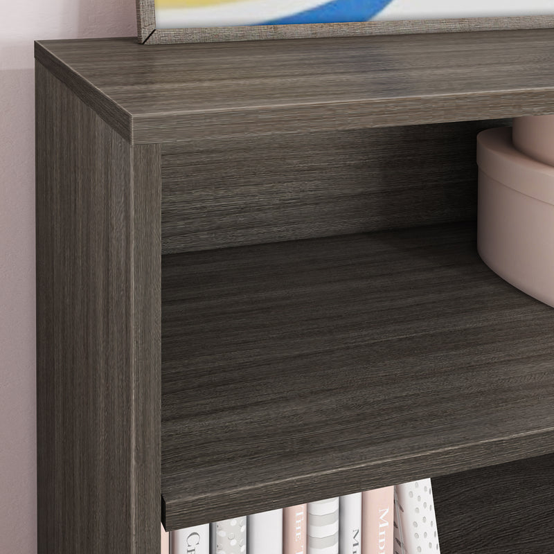 Close-up of dark grey wood bookshelf with textured grain, modern shelving and styling featuring a round pink storage box and pastel-spined books.