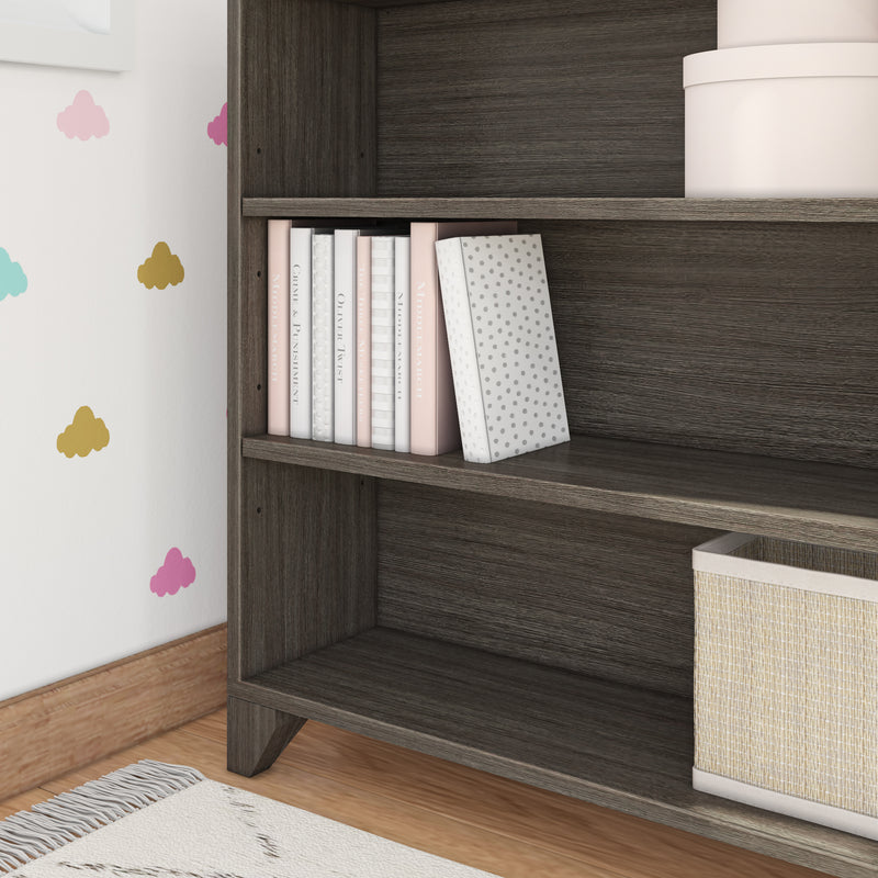 Dark wood nursery bookshelf with pastel children's books, polka-dot bookend, cloud wall decals and woven storage basket