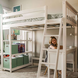 Child smiling at desk under white loft bed in organized playroom with storage shelves.