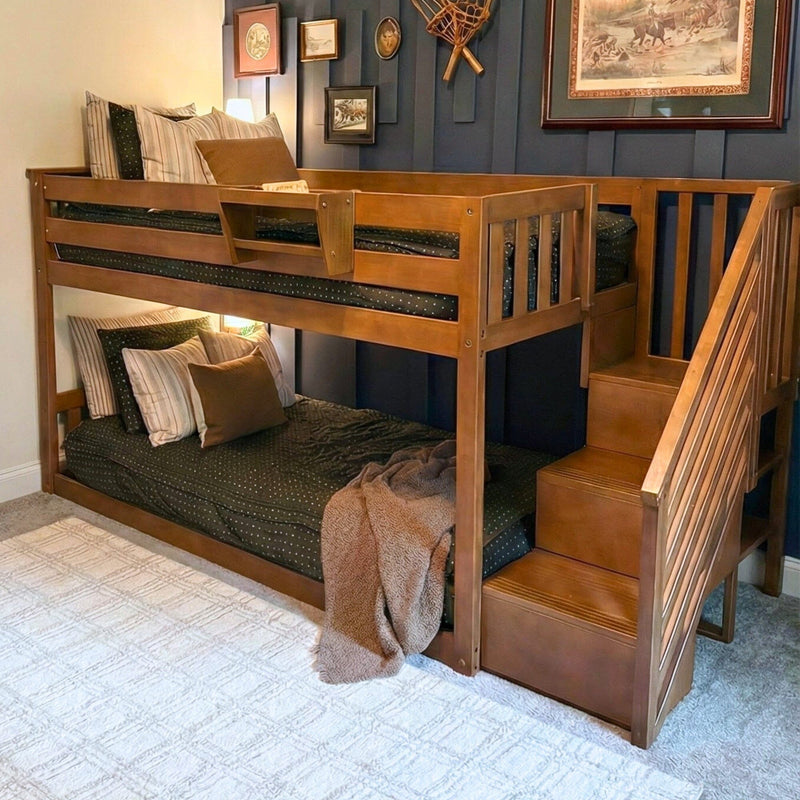 Solid wood twin-over-full bunk bed with built-in staircase storage, dark green bedding and striped pillows against navy accent wall in a cozy kids' bedroom